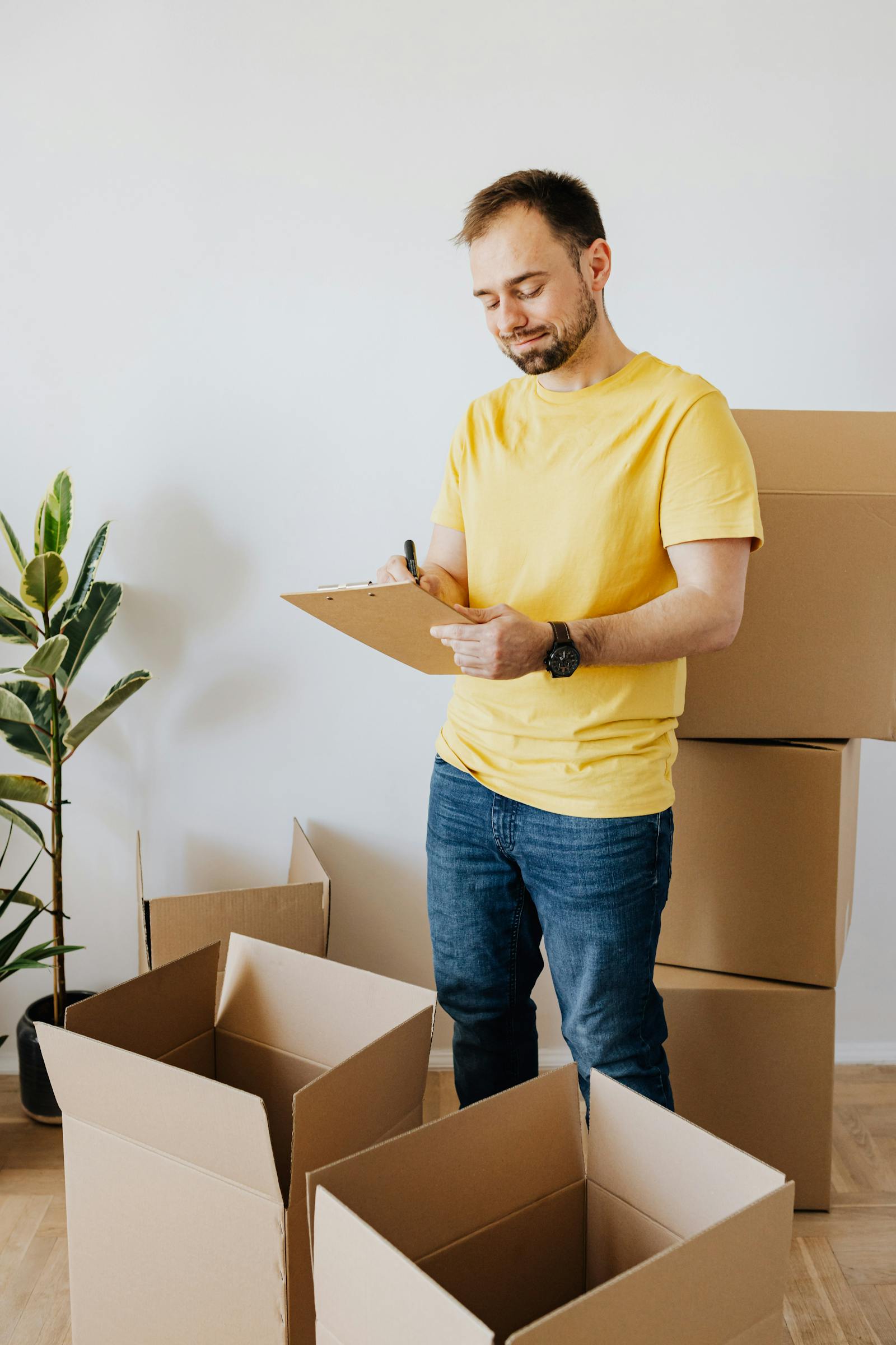 Man comparing moving quotes on a clipboard next to cardboard boxes