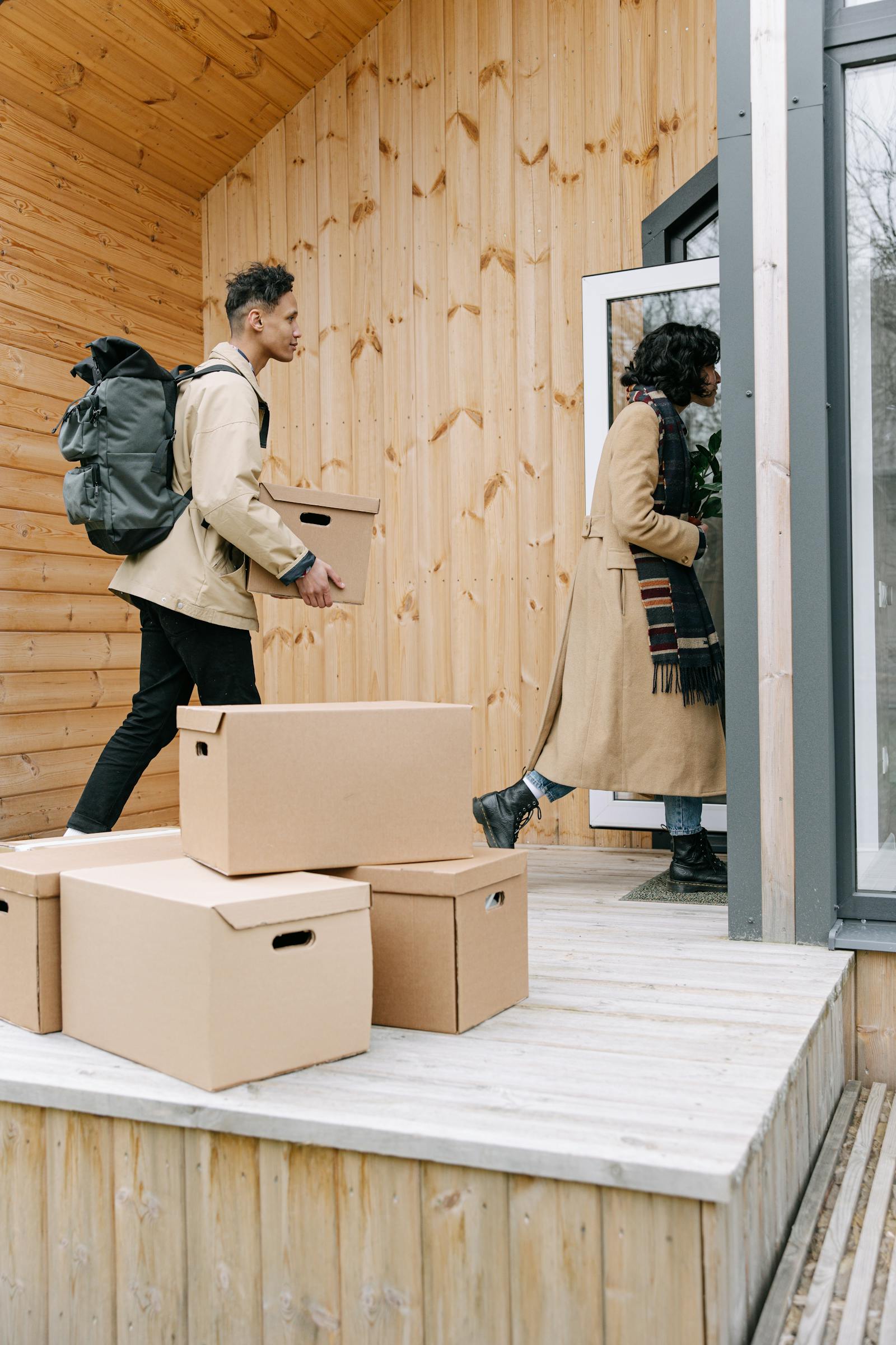 A man and woman carrying cardboard boxes into their new house