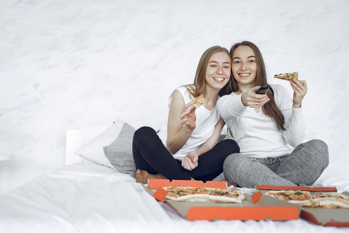 Two roommates enjoying pizza and watching TV together in their shared apartment